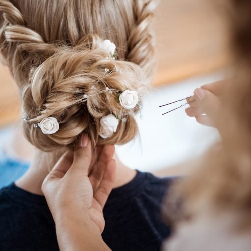 Female hairdresser making hairstyle to beautiful blonde girl in beauty salon. Copy space.