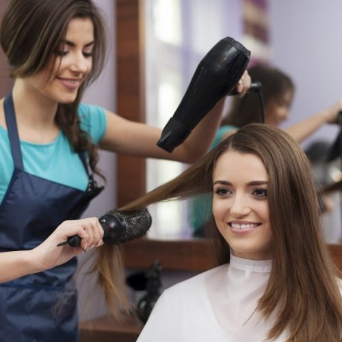 Female hairdresser using hairbrush and hair dryer