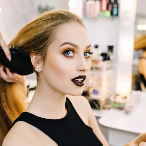 Stylish portrait of attractive young woman in beauty salon preparing to party. Making hairstyle, makeup, stylist, professional, cheerful mood, hairdressing service, looking to camera